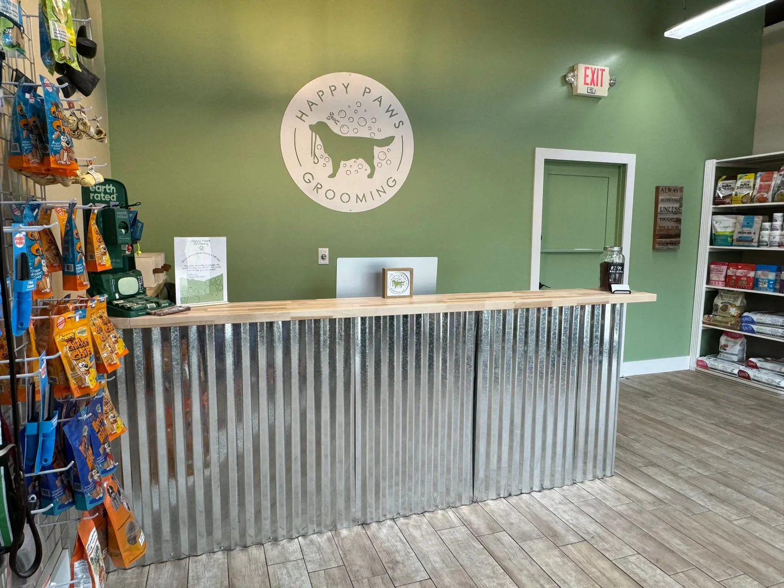 The Happy Paws front desk with the logo on a sage green wall, treats and dog food on the shelves